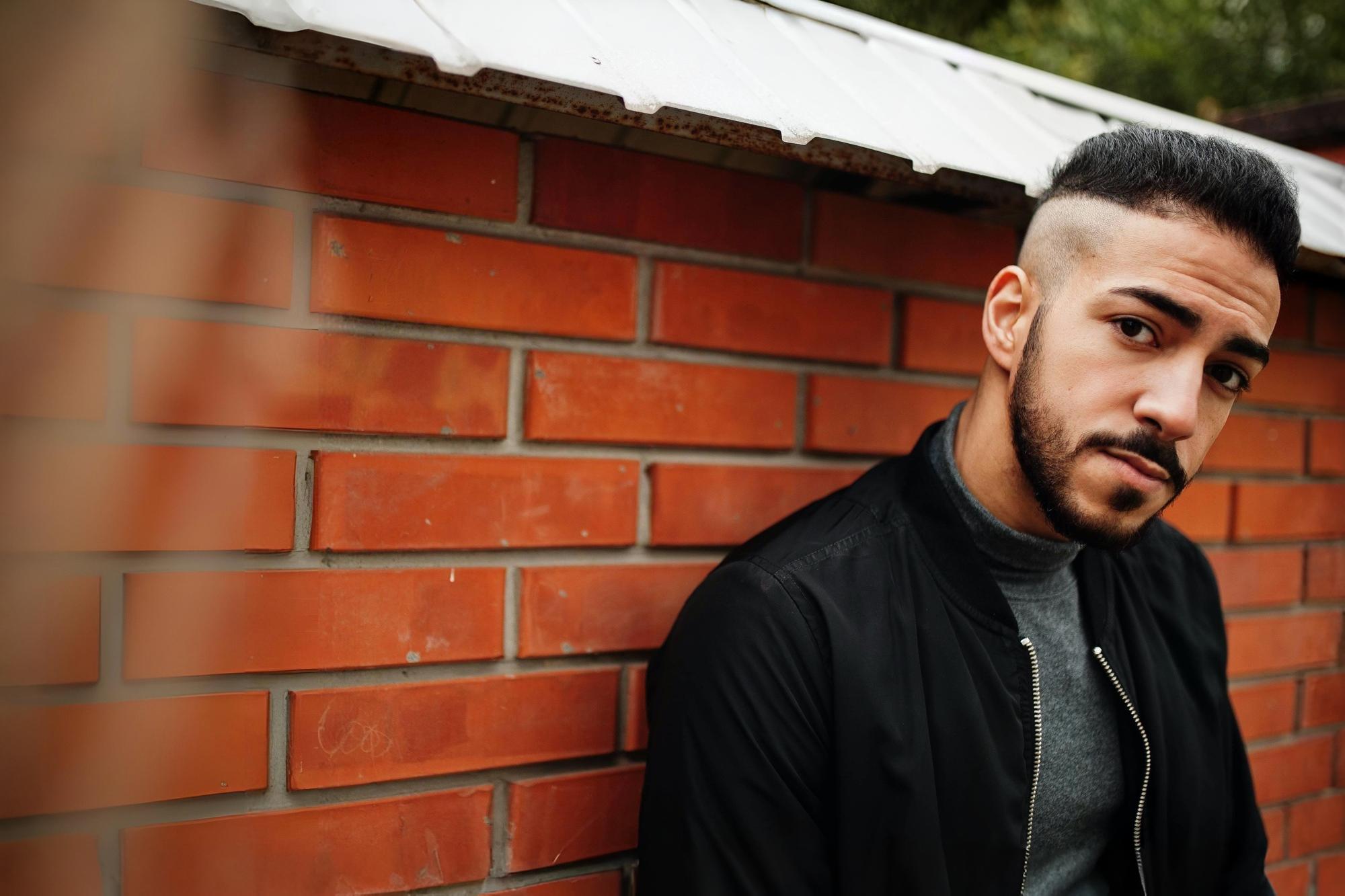 Man sitting quietly against a brick wall, reflecting on faith and wondering if he truly belongs as a child of God.