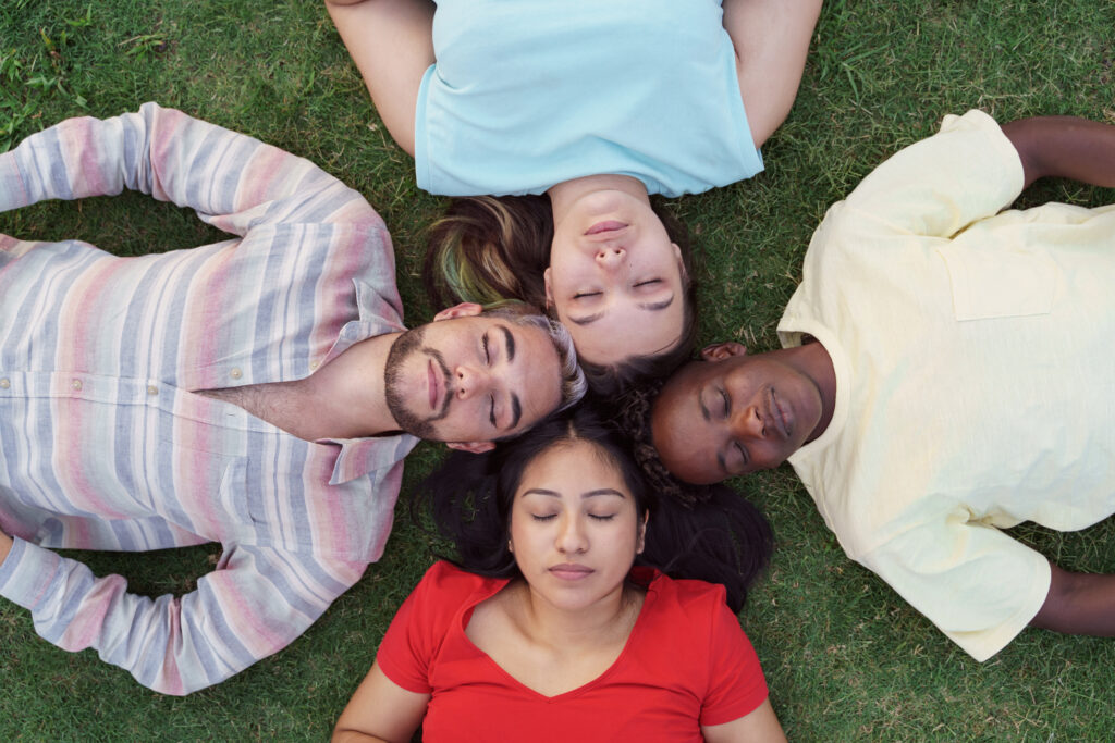 Group of diverse friends resting peacefully on grass, symbolizing unity, identity, and belonging as sons and daughters of God.