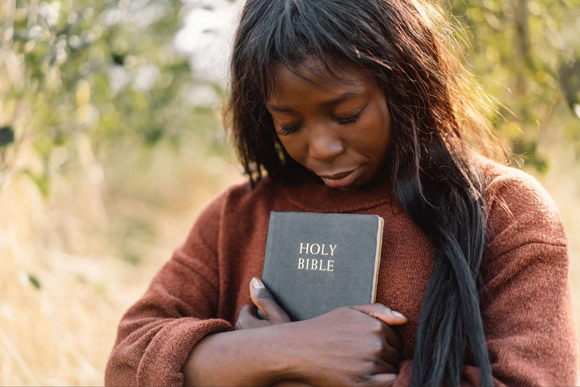 Woman holding a Bible close to her heart, reflecting on faith and God’s presence during a season of silence.