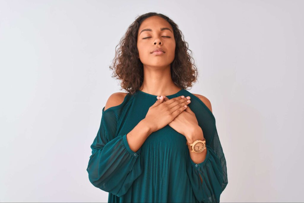 Peaceful woman with eyes closed and hands over heart, representing inner alignment, prayer, and living spirit first with God’s presence.