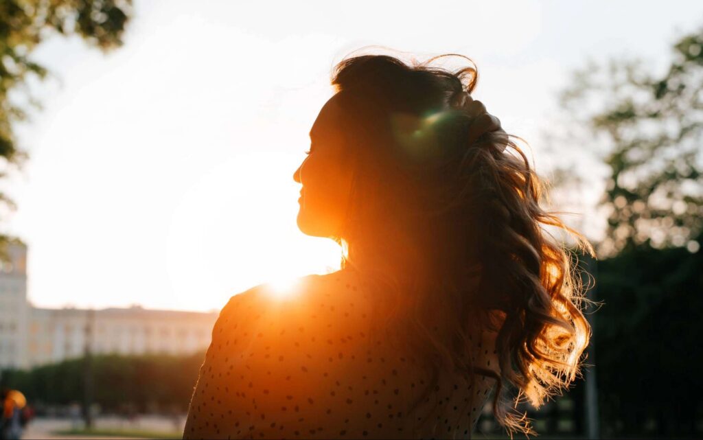 Woman standing in warm sunlight with a peaceful expression, representing holy boldness flowing from union with God rather than striving