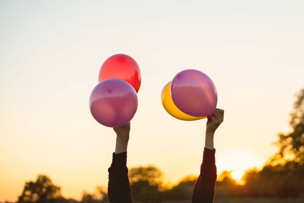 Hands lifting colorful balloons toward the sky, representing agreement with God and making room for more of Christ.