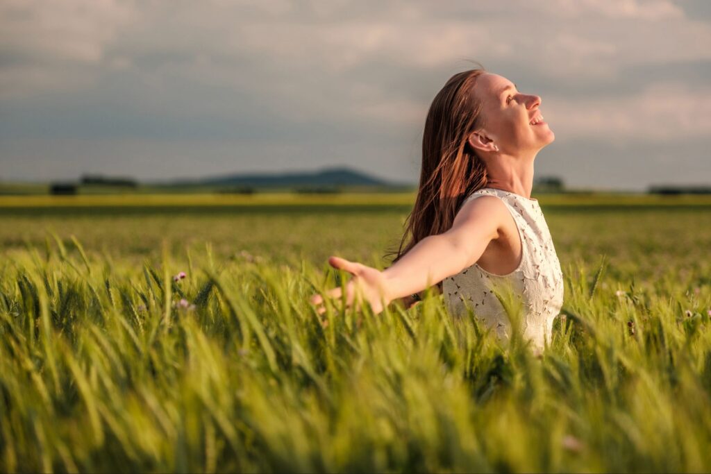Woman standing in an open field with arms outstretched, symbolizing surrender and making room for more of Christ.